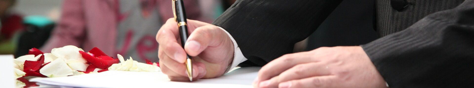 Eine männliche Hand unterschreibt eine Heiratsurkunde.